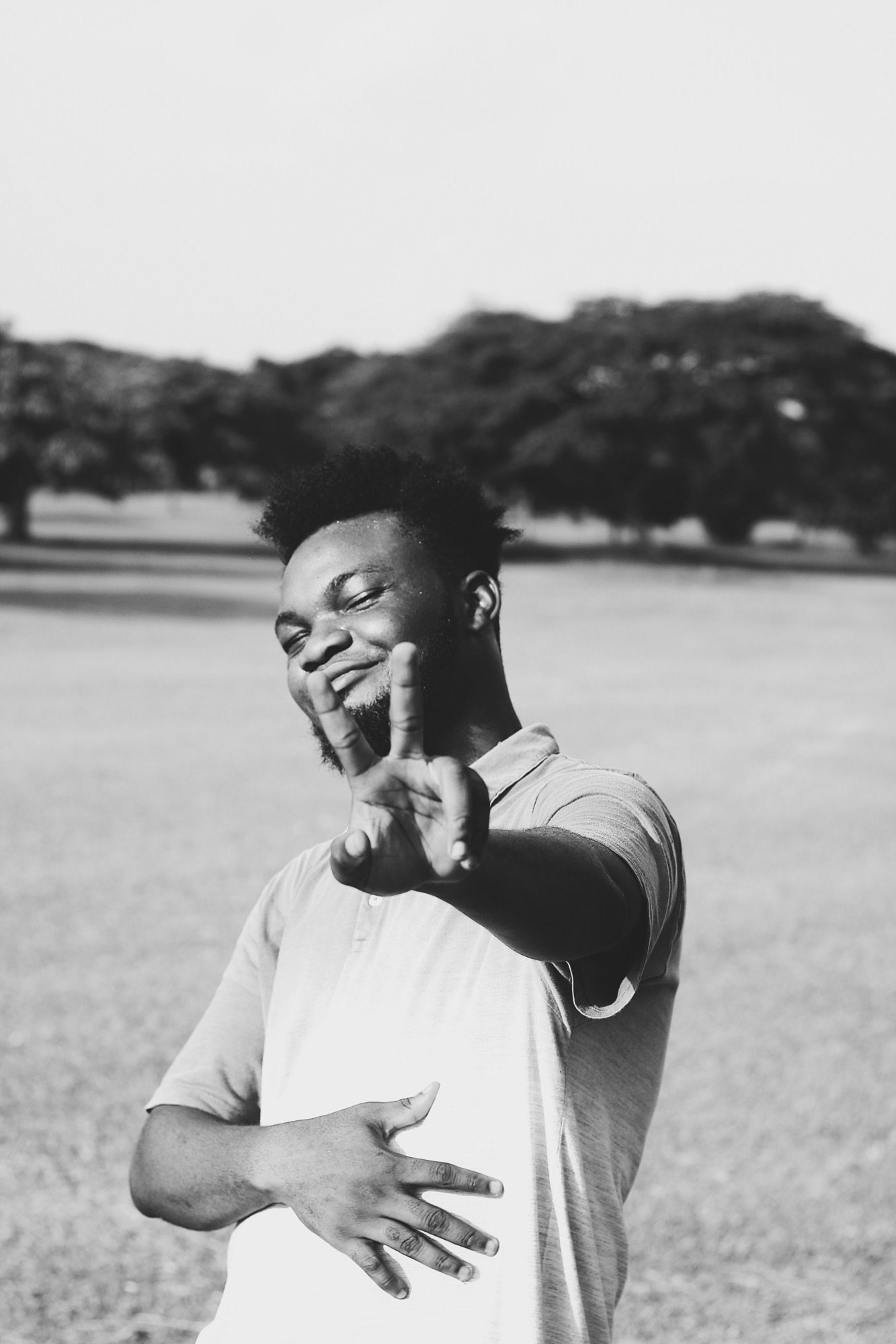A young man smiling freely in an open field, one hand resting on his stomach