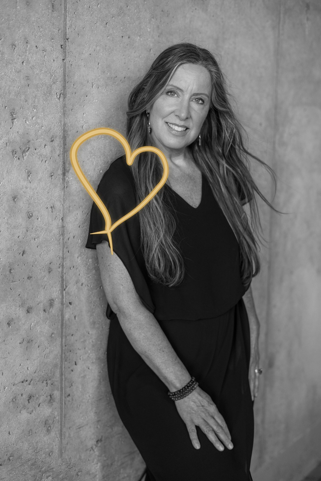 Lisa Watson smiling against a concrete wall beside a gold heart